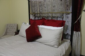 A bed with a metal headboard, white bedding, and red pillows.