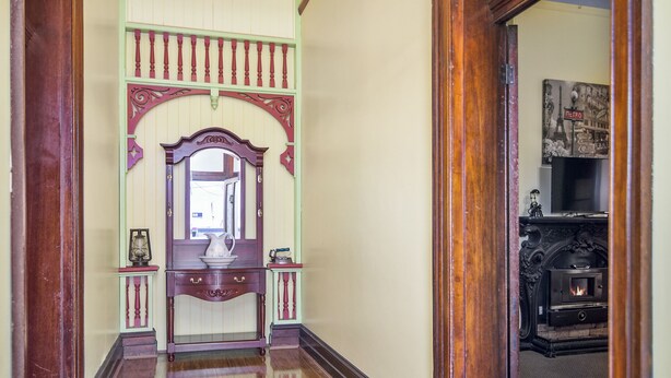 Un couloir doté d’un plancher en bois, d’une arche décorative aux couleurs verte et rouge, d’un miroir et d’une cheminée sur laquelle est posée une télévision.