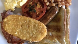 Une assiette de nourriture pour le petit-déjeuner comprenant des œufs, des haricots, des tomates, des toasts et du bacon.