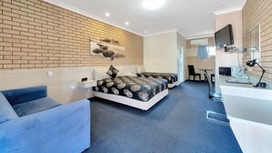 Une chambre d’hôtel moderne avec un mur décoré d’un motif en briques, un grand lit avec une literie à motifs, un canapé bleu, un bureau avec un ordinateur et un téléviseur à écran plat.