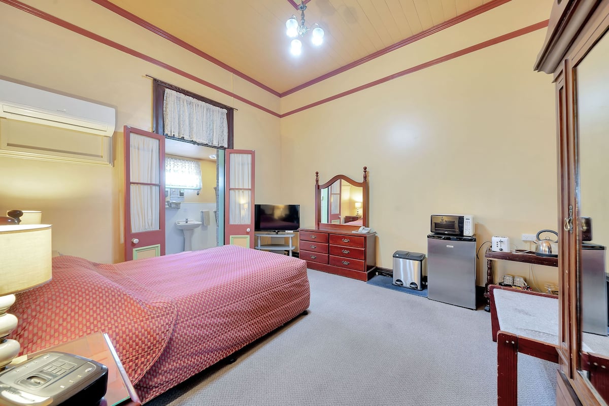 Habitación de hotel con cama, cómoda, televisor, microondas y una kitchenette pequeña.