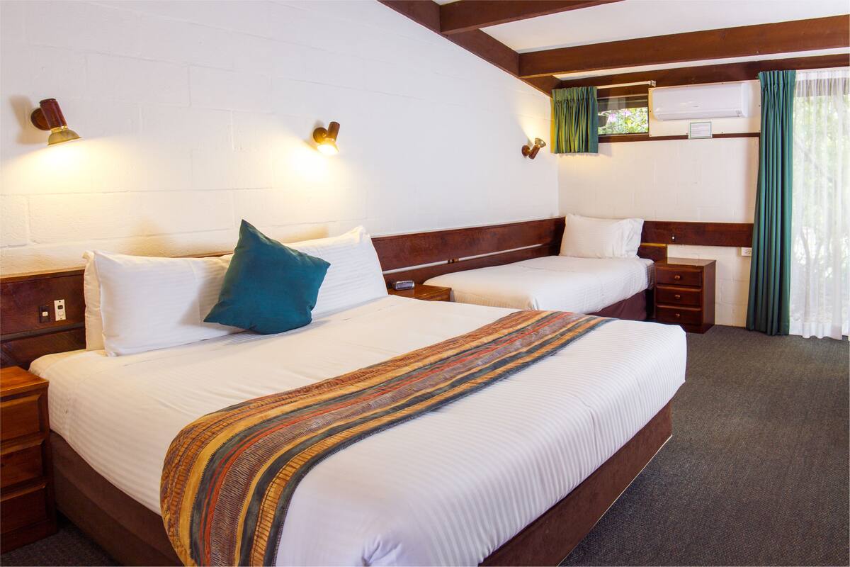 A hotel room with two beds, wooden headboards, white bedding, and a striped throw blanket.