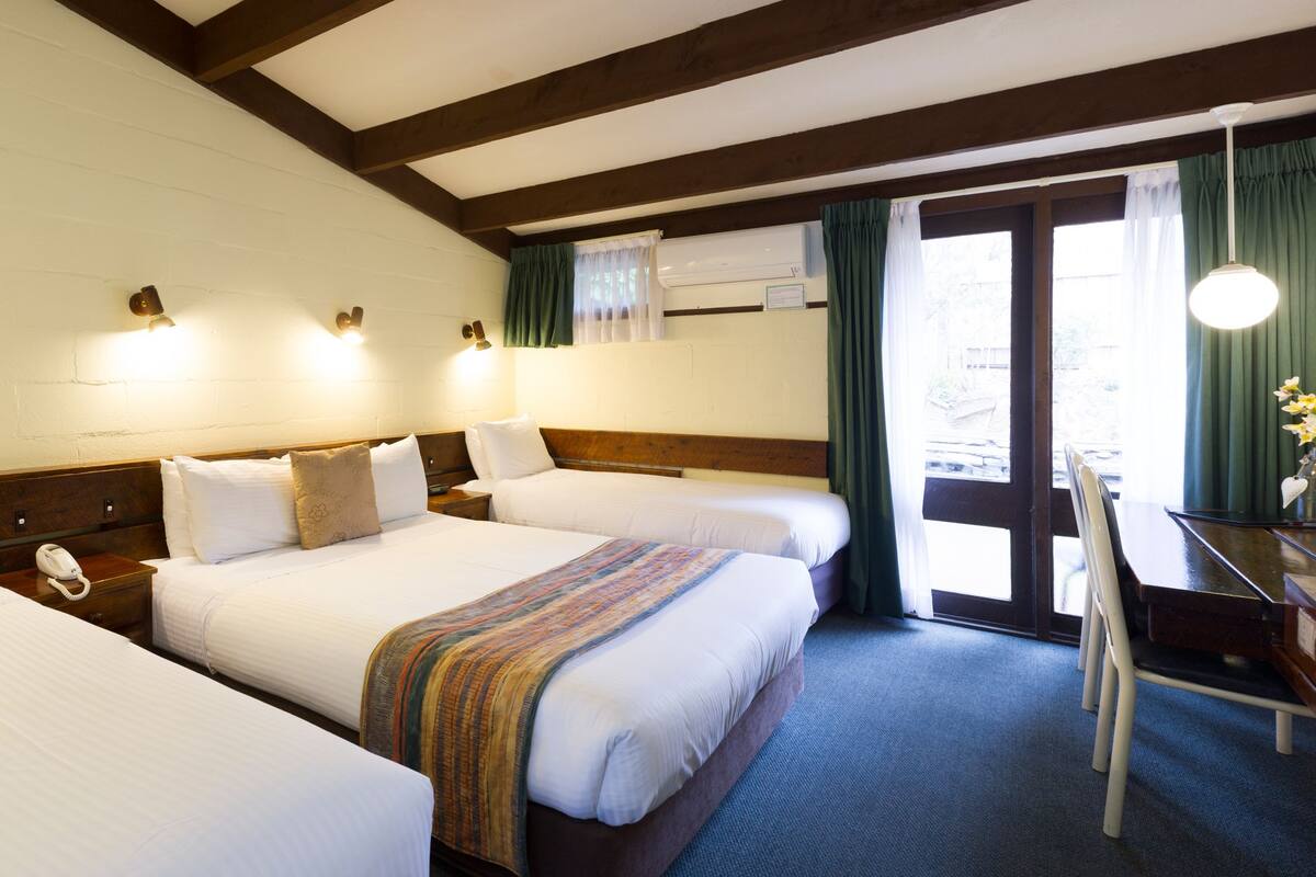 A hotel room with three beds, a desk with a chair, and a view of the outdoors.