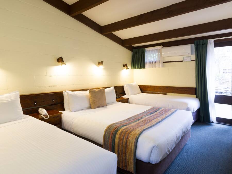 Habitación de hotel con tres camas, un escritorio con silla y vistas al exterior.