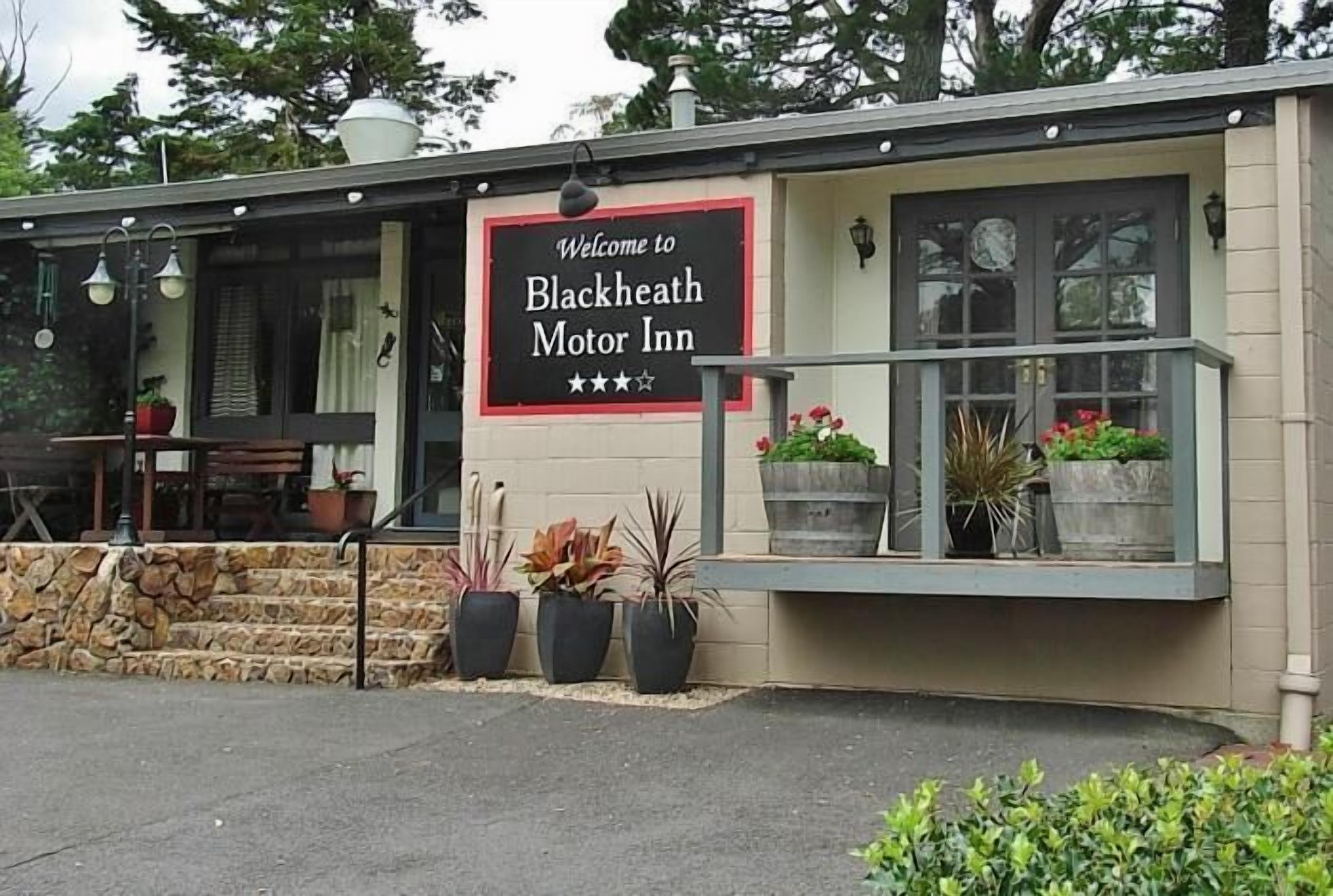The exterior of Blackheath Motor Inn with a welcome sign, outdoor seating, and potted plants.
