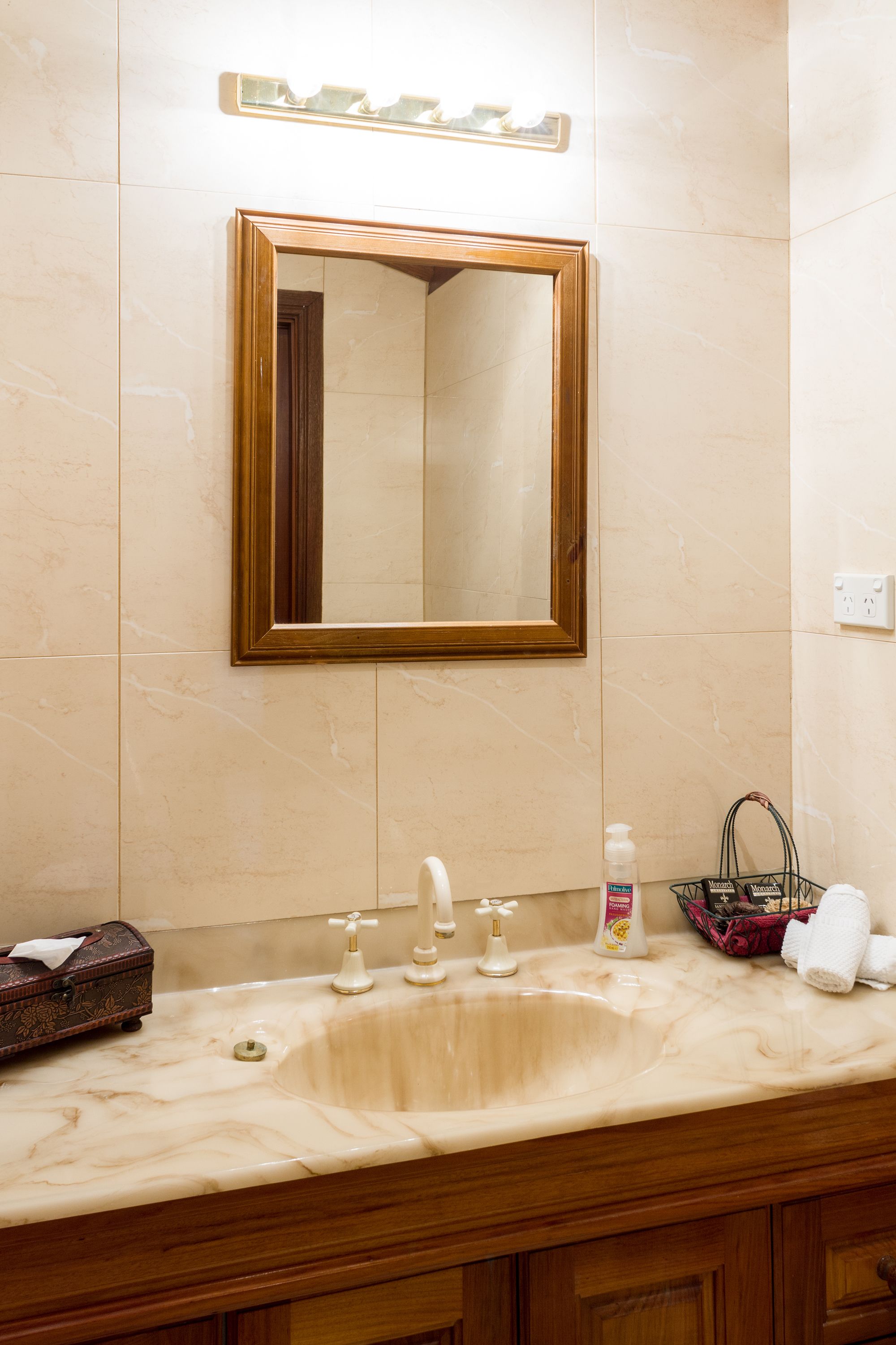 A bathroom with a marble sink, a wooden-framed mirror, and a small basket with toiletries.