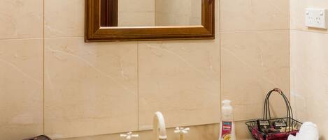 Un baño con un lavabo de mármol, un espejo con marco de madera y una pequeña cesta con artículos de aseo.