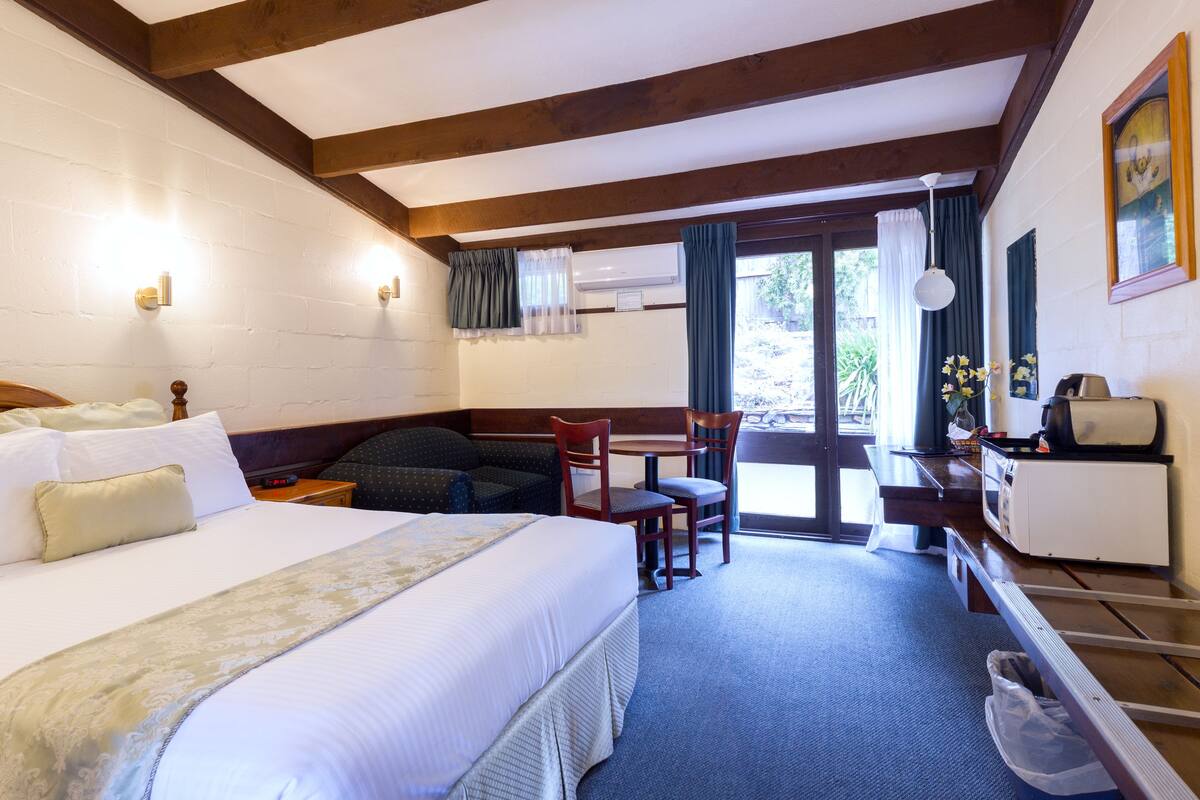 A hotel room with a large bed, a desk, a chair, and a view of the outdoors through a door.