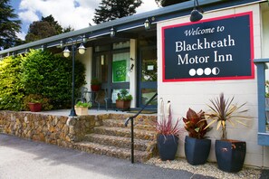 Het uiterlijk van Blackheath Motor Inn, met een welkomstbord, stenen trappen, potplanten en een overdekt terras.