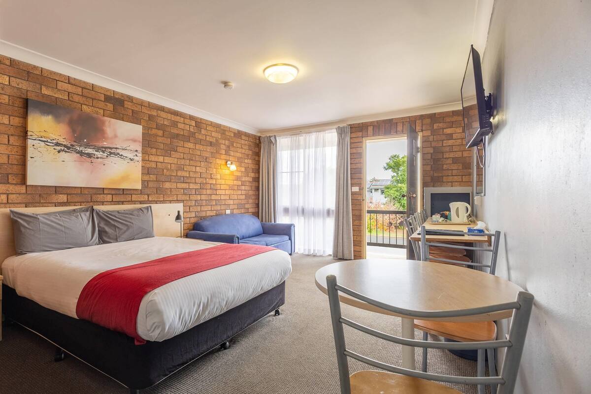 Una habitación de hotel con una cama grande, un escritorio, una silla, un televisor y un balcón con cortinas.