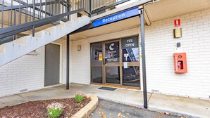 A hotel reception with a staircase leading to an upper floor, a fire extinguisher mounted on the wall, and a sign indicating the reception hours. - Comfort Inn Dubbo City (Dubbo)