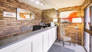 A reception area with a brick wall, a reception desk, a chair, a lamp, and a painting. - Comfort Inn Dubbo City (Dubbo)