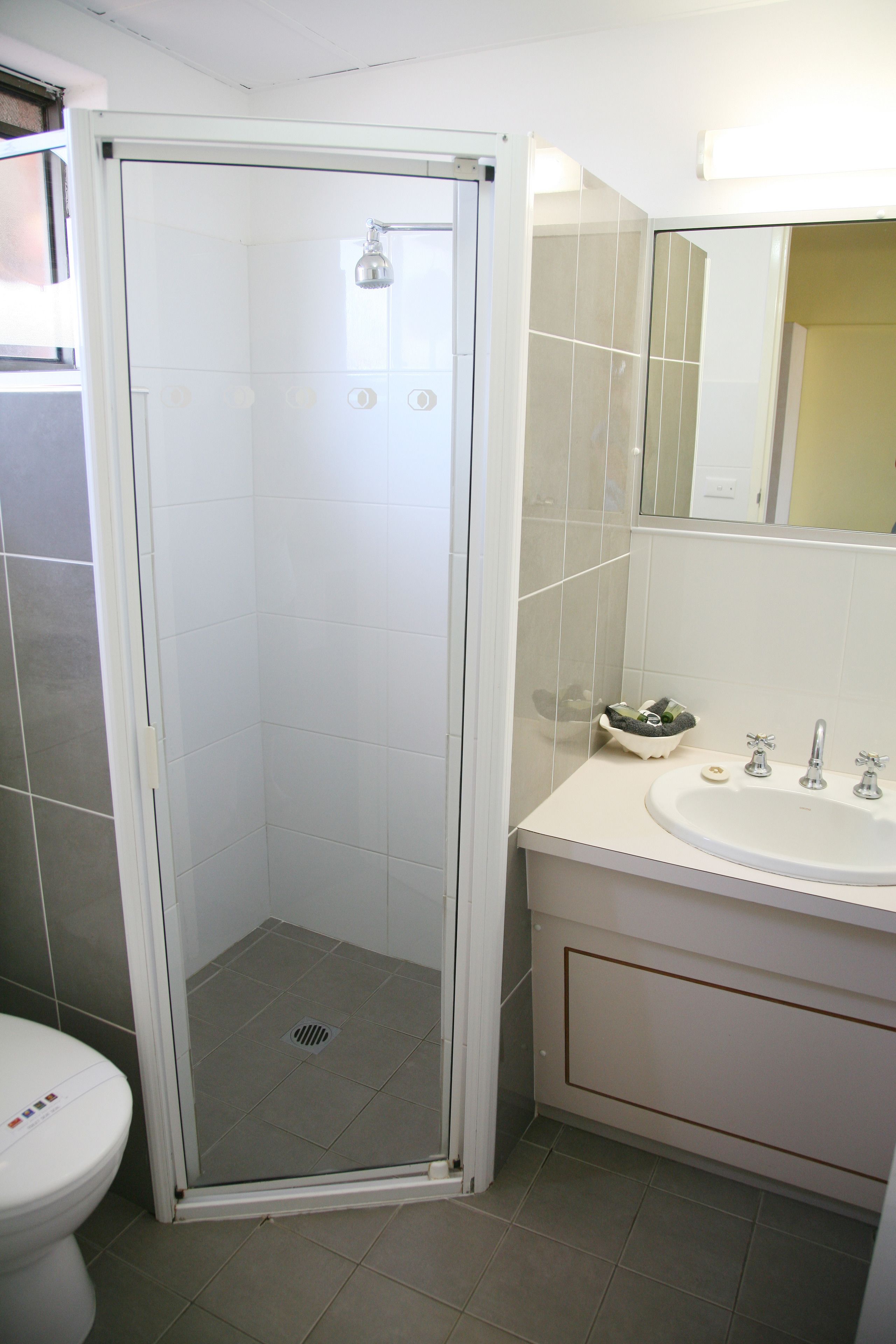 Un bagno con cabina doccia in vetro, un water e un lavandino con specchio sopra.