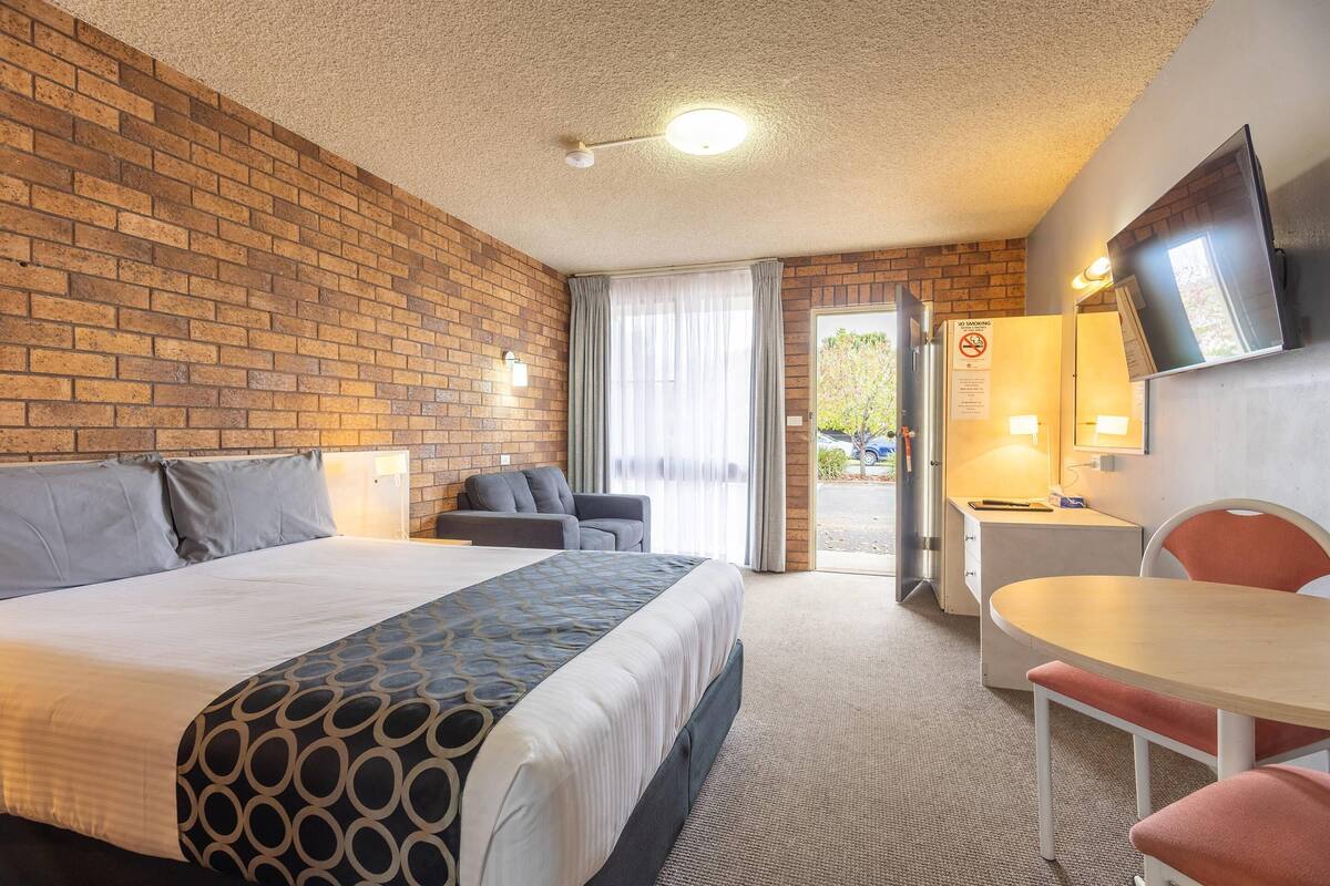 Habitación de hotel con pared de ladrillo, cama con cubrecama estampado, escritorio y silla, y televisión en la pared.