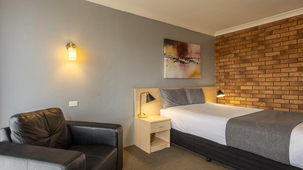 A hotel room with a bed, a nightstand, a lamp, a couch, and a brick wall. - Comfort Inn Dubbo City (Dubbo)