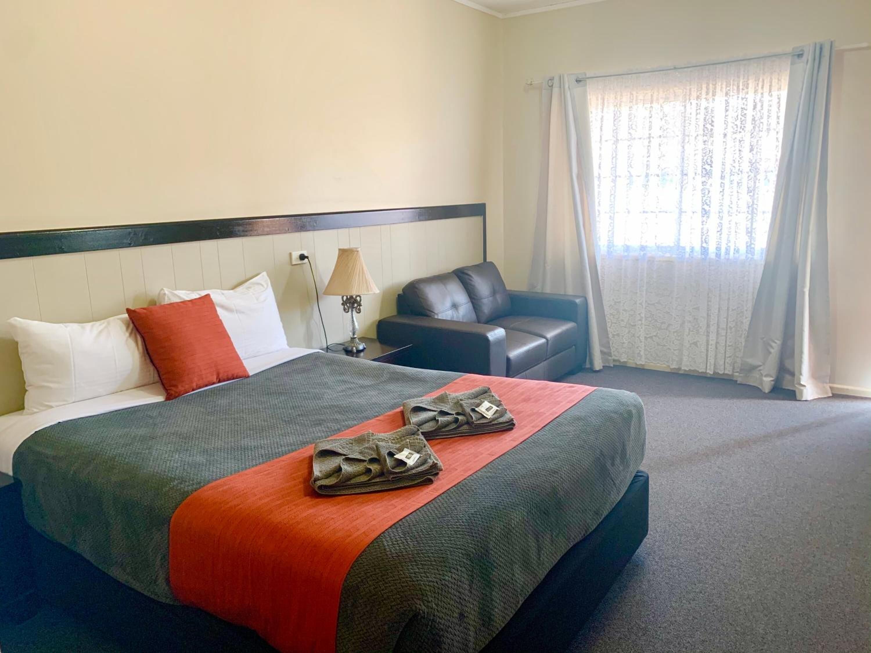 Una habitación de hotel con cama, escritorio, silla y ventana con cortinas.