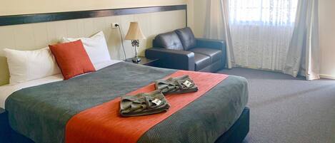 Una habitación de hotel con cama, escritorio, silla y ventana con cortinas.