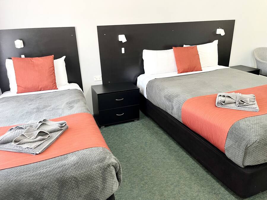 Zwei Betten mit schwarzen Kopfteilen, Bettwäsche in Grau und Orange, ein graues Handtuch und ein Nachttisch mit Schubladen in Schwarz.