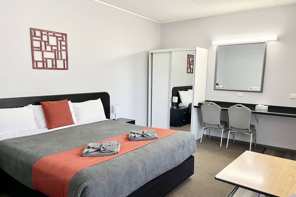 Una habitación de hotel con cama, escritorio, silla, espejo y armario.