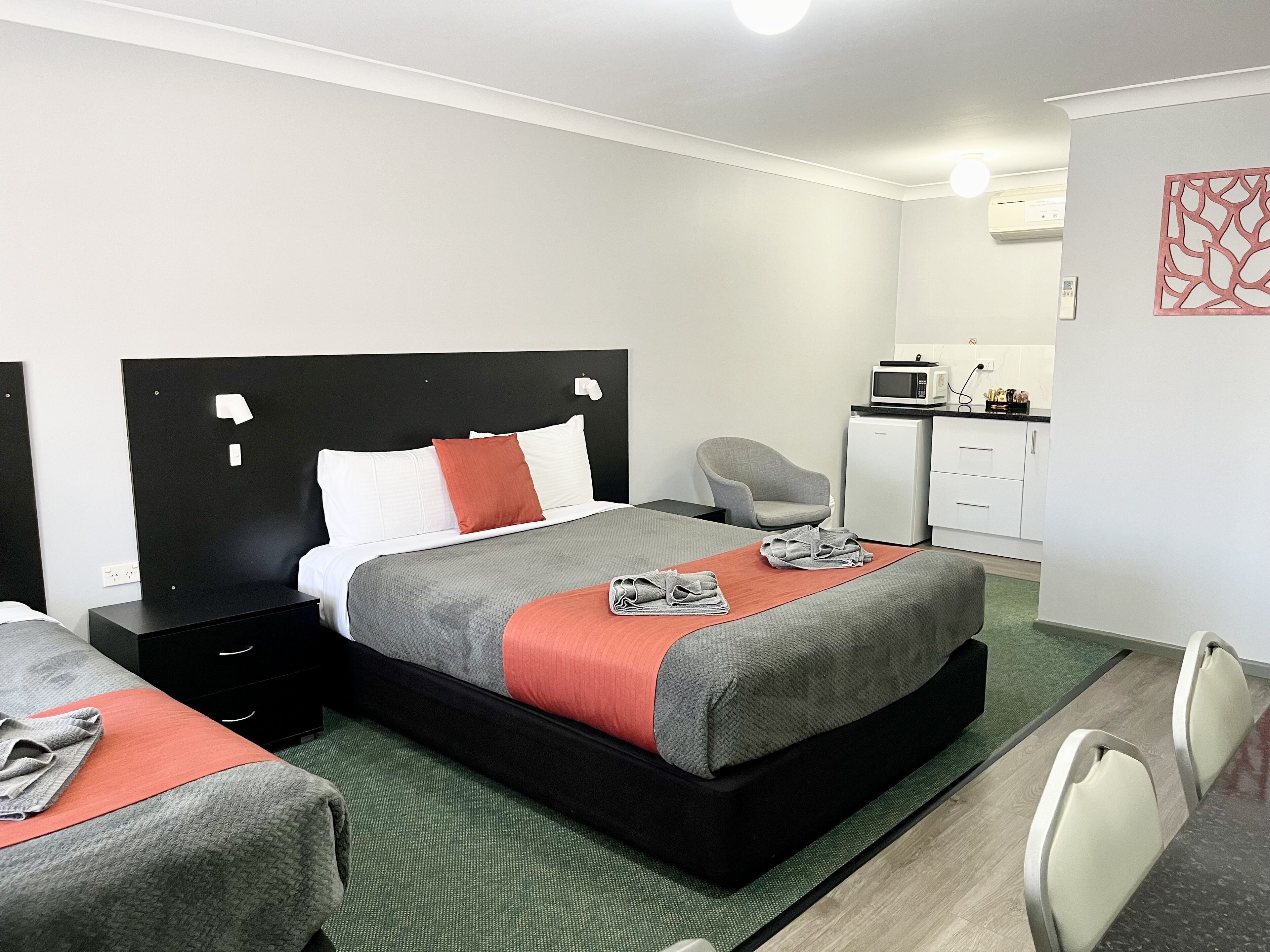 Habitación de hotel con cama, escritorio, silla, microondas y una pequeña cocina.