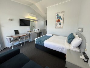 A hotel room with a bed, a desk, a chair, a television, and a painting on the wall.