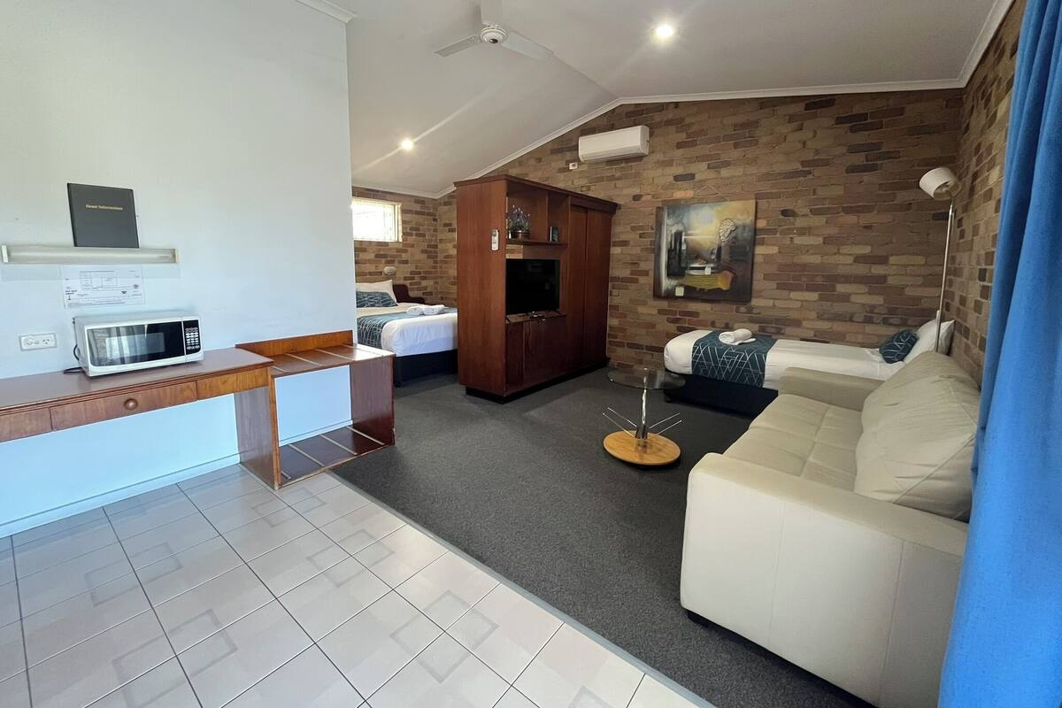 A modern hotel room with a kitchenette, a sofa, a bed, and a brick wall.