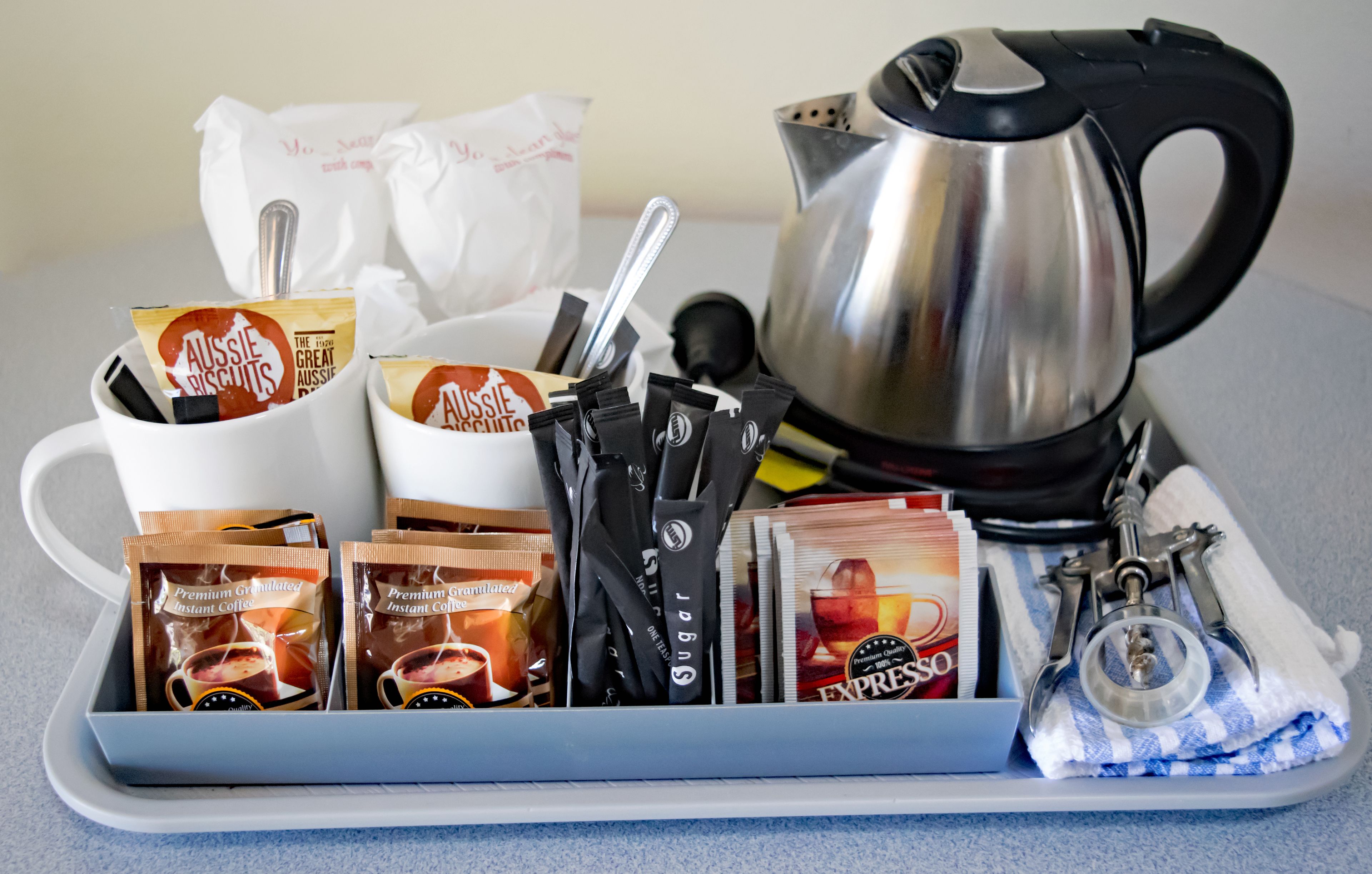 A tray with instant coffee packets, sugar packets, a spoon, a tea kettle, and a pair of scissors.