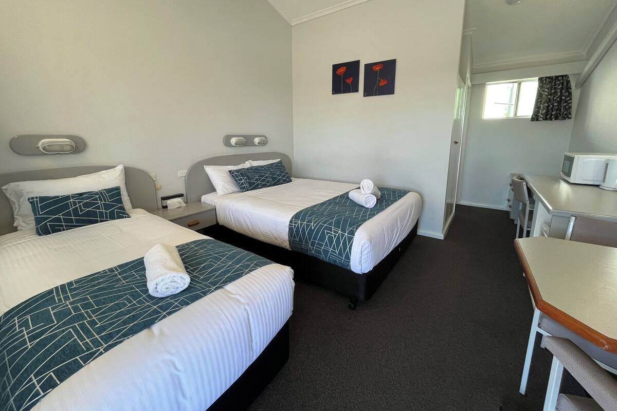 A hotel room with two beds, a desk, a microwave, and a window.