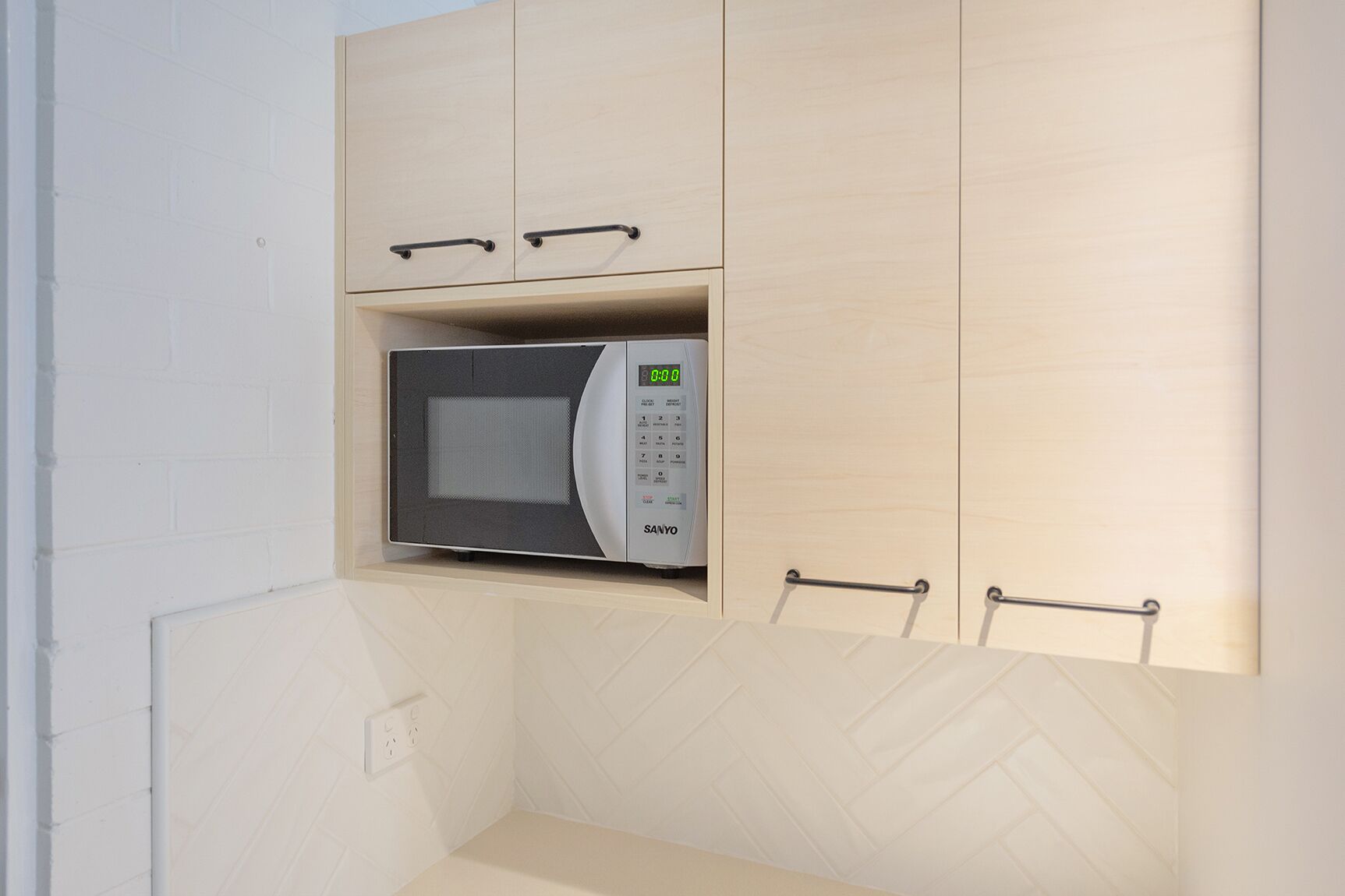 Un microondas en una cocina con armarios de madera clara y un salpicadero blanco tipo espiga.