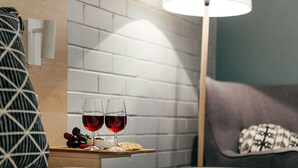 A neatly arranged table with two glasses of red wine, a cheese platter, and a lamp in a modern room with a brick wall and a grey sofa. - Fitzroy Motor Inn Grafton (Grafton)