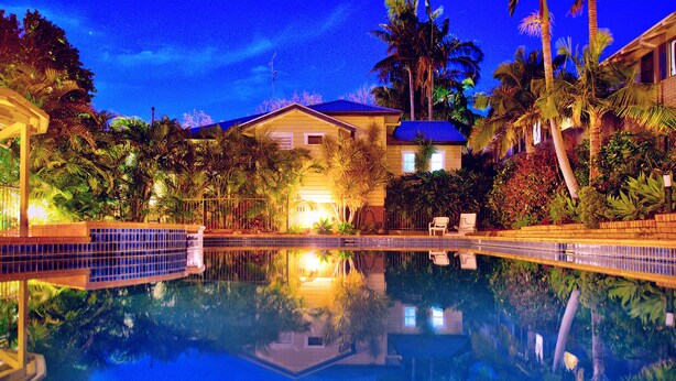 A nighttime swimming pool with clear water reflecting the surrounding buildings and palm trees. - Fitzroy Motor Inn Grafton (Grafton)