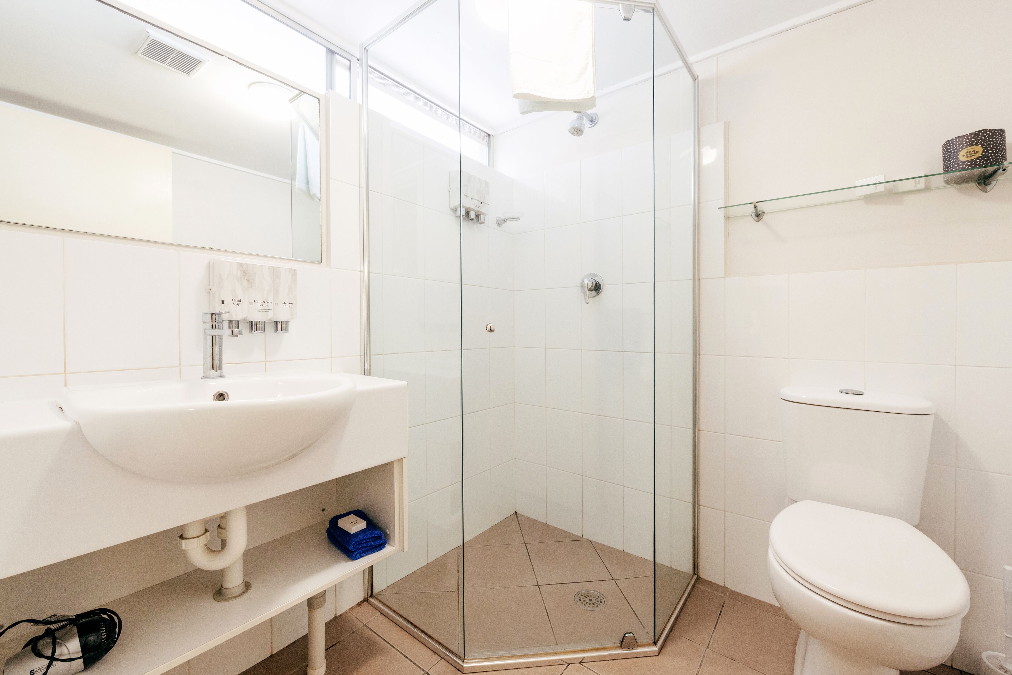 A modern bathroom with a glass-enclosed shower, white tiles, a sink with a mirror, and a toilet.