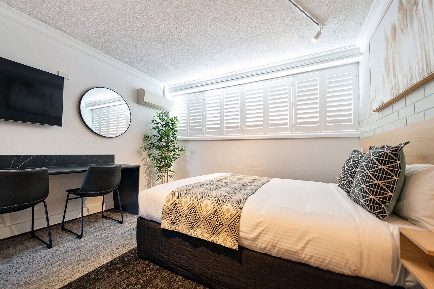 Quarto moderno com cama, mesa de cabeceira e escrivaninha com cadeiras.