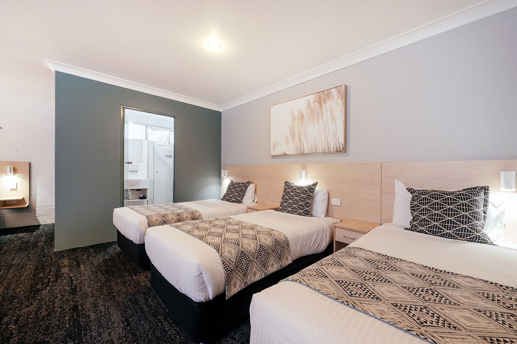A hotel room with two beds, a large window, a bathroom, and a painting on the wall.