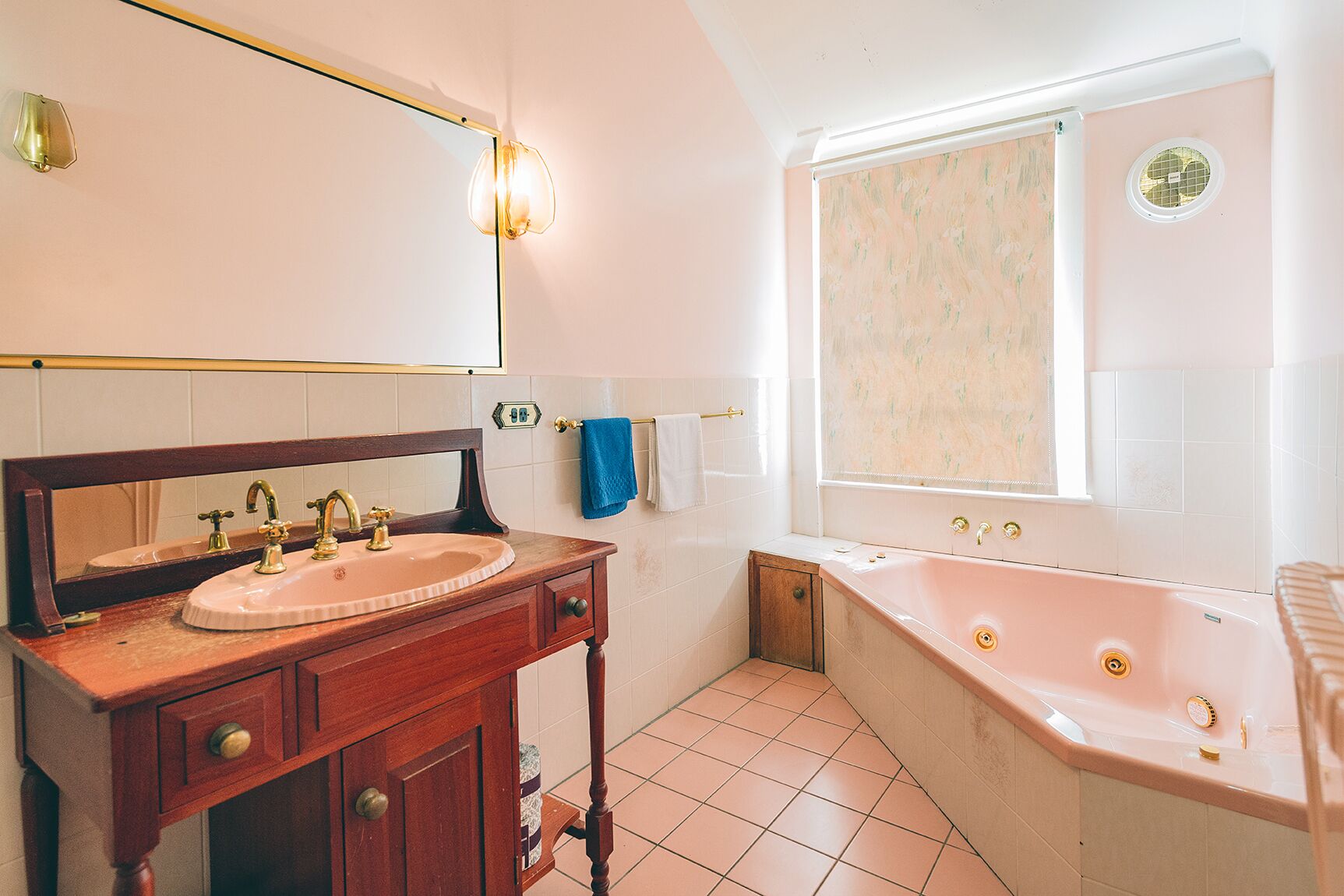 A bathroom with a wooden vanity, a sink, a mirror, a bathtub, and a window with a shower curtain.