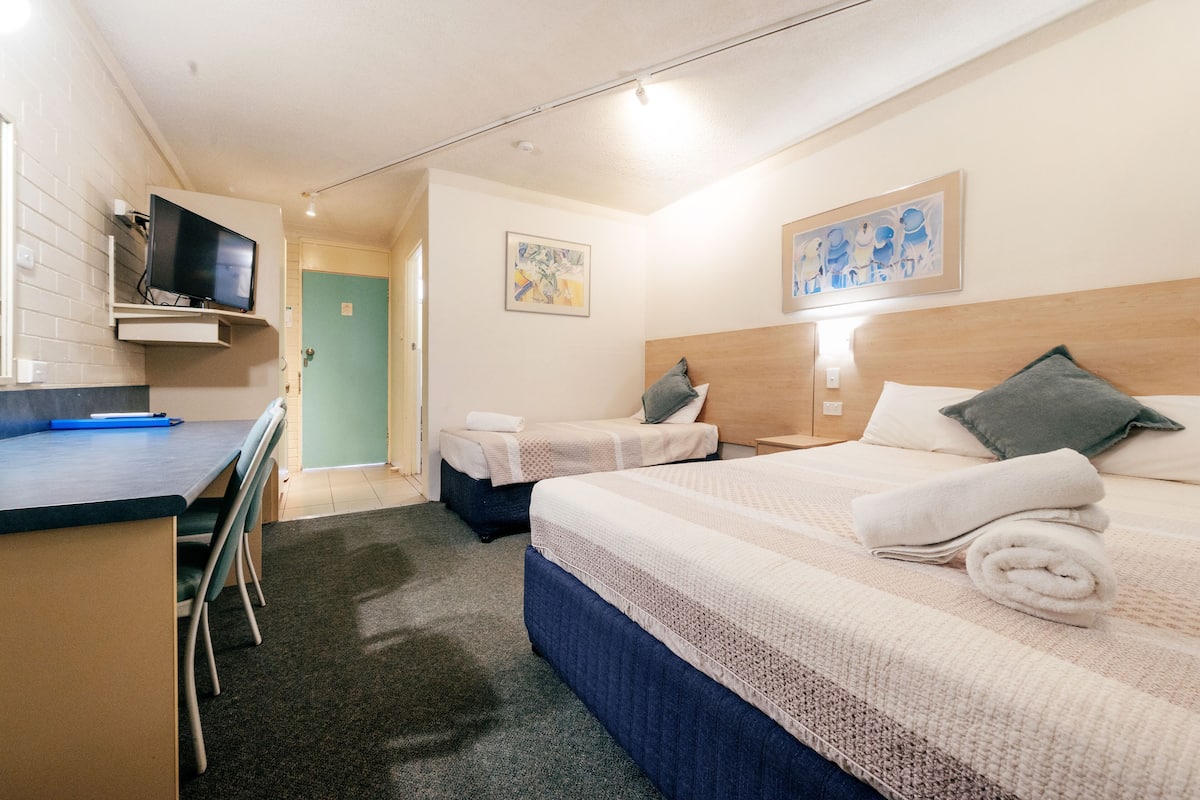 A hotel room with a bed, bedside table, and a desk with a chair.