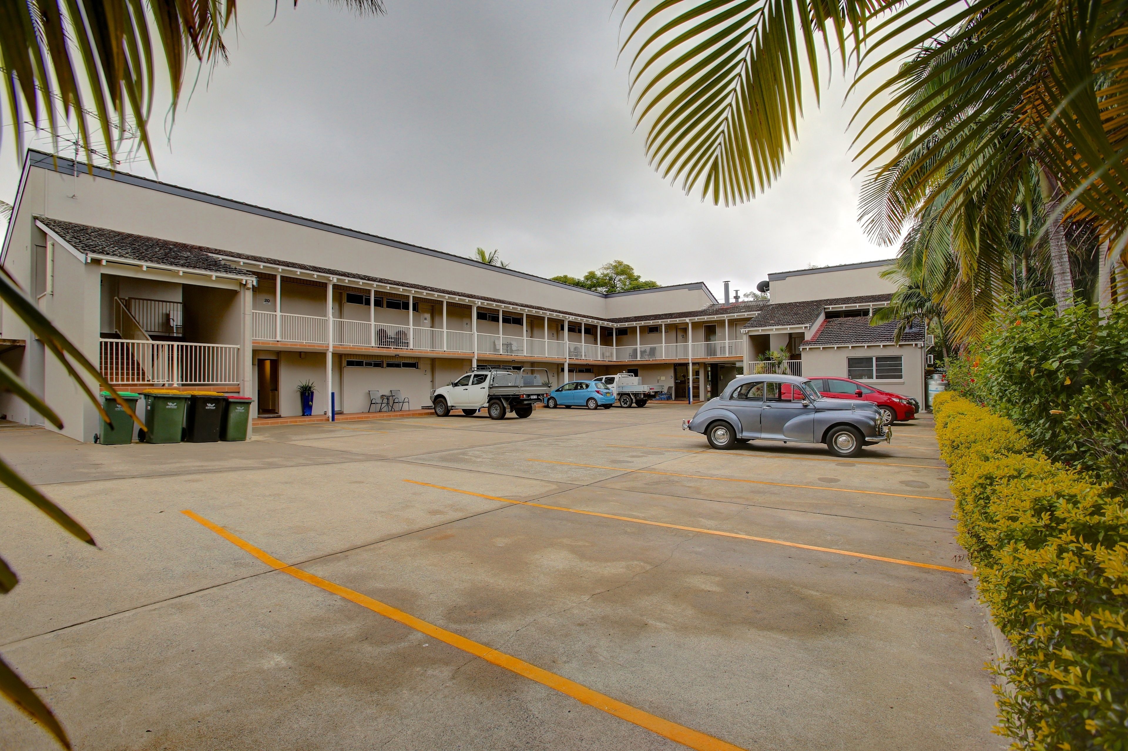 Un motel con estacionamiento, varios pisos y un área exterior techada.
