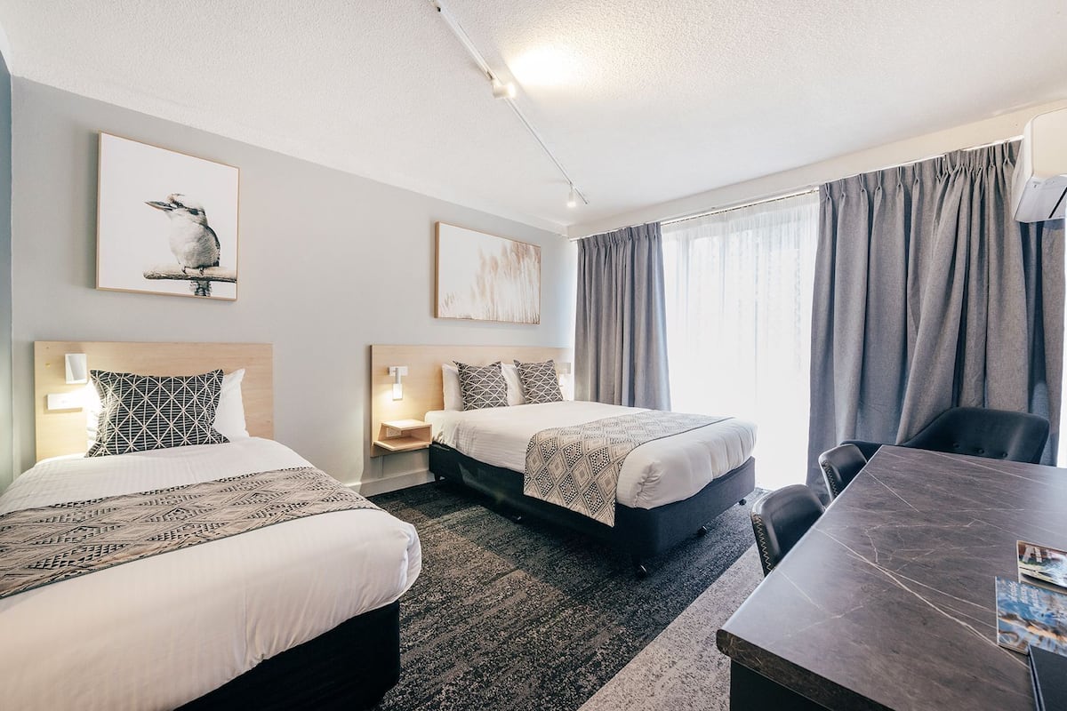 A hotel room with two beds, a desk, and a large window with curtains.