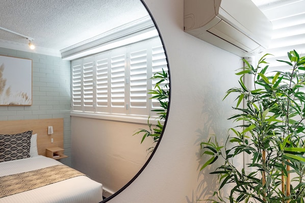 A bedroom with a bed, a nightstand, a bedside table, a window with blinds, and a potted plant. - Fitzroy Motor Inn Grafton (Grafton)