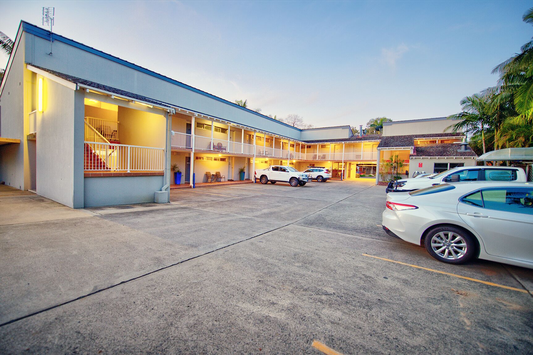 Un motel con un patio central, varios balcones y un estacionamiento con varios autos.