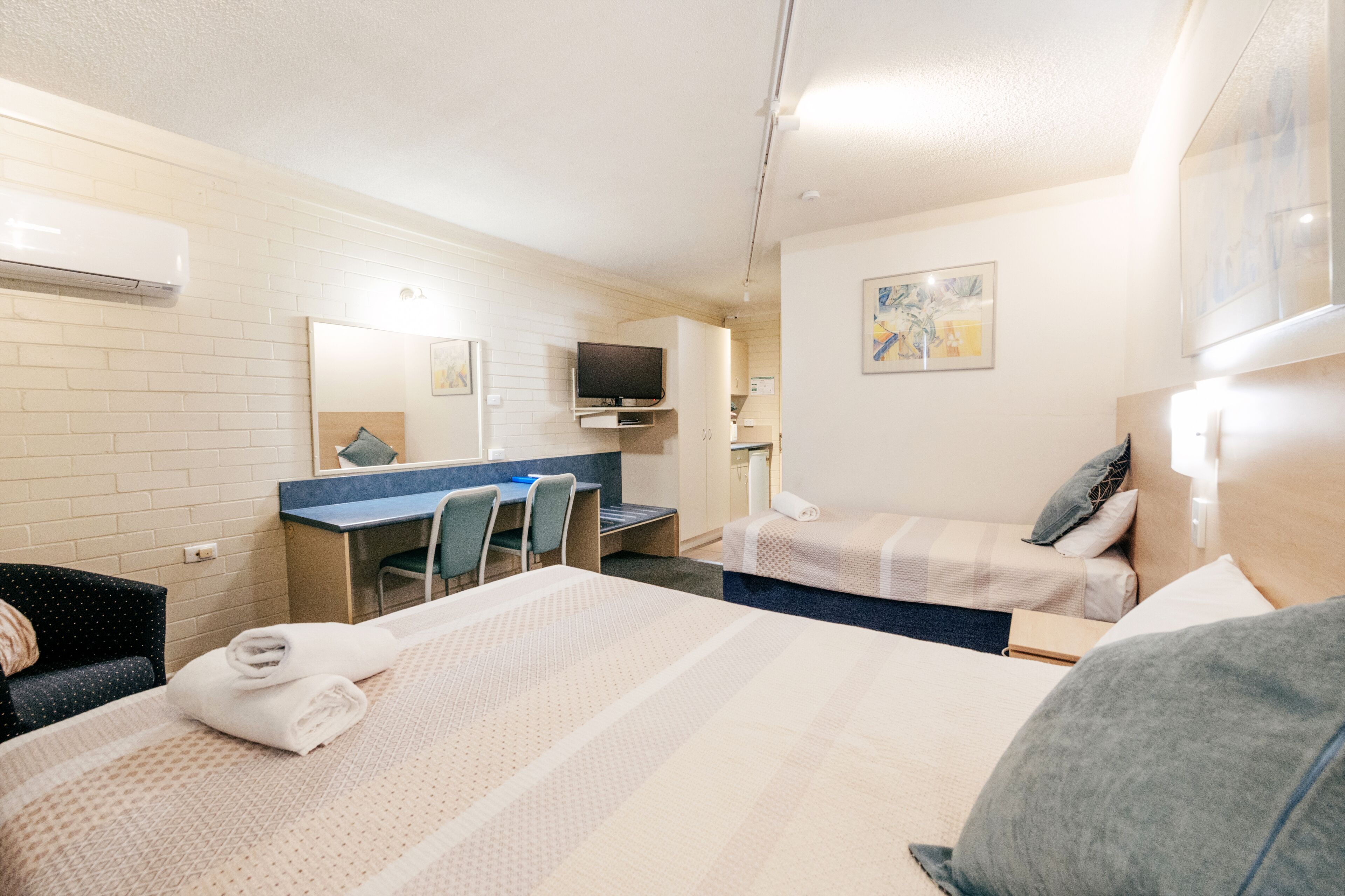A hotel room with two beds, a desk, a chair, a television, and a bathroom.