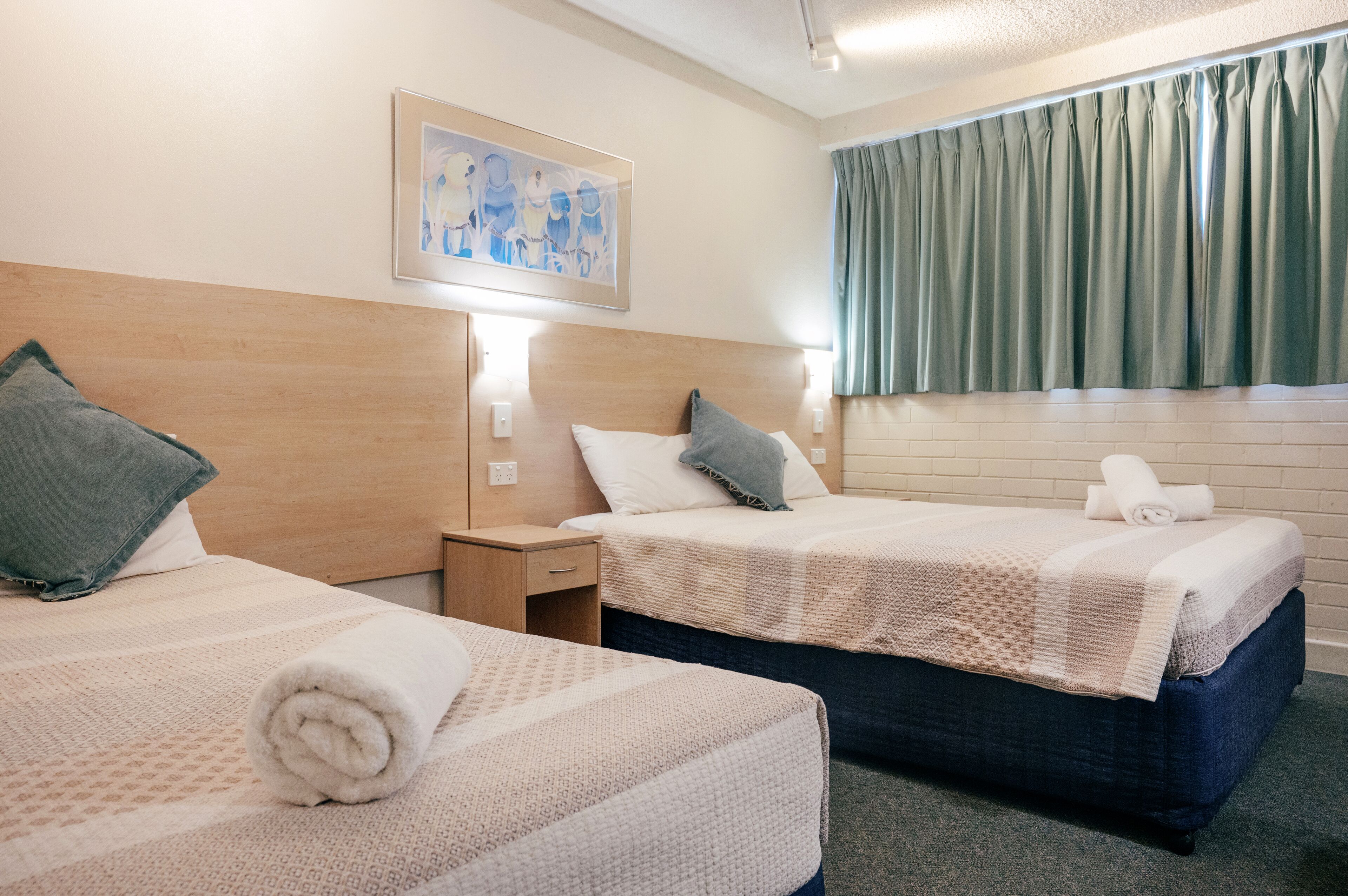 Habitación de hotel con dos camas, una mesita de noche, un cuadro en la pared y una ventana con cortinas.