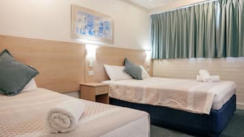 Habitación de hotel con dos camas, una mesita de noche, un cuadro en la pared y una ventana con cortinas.