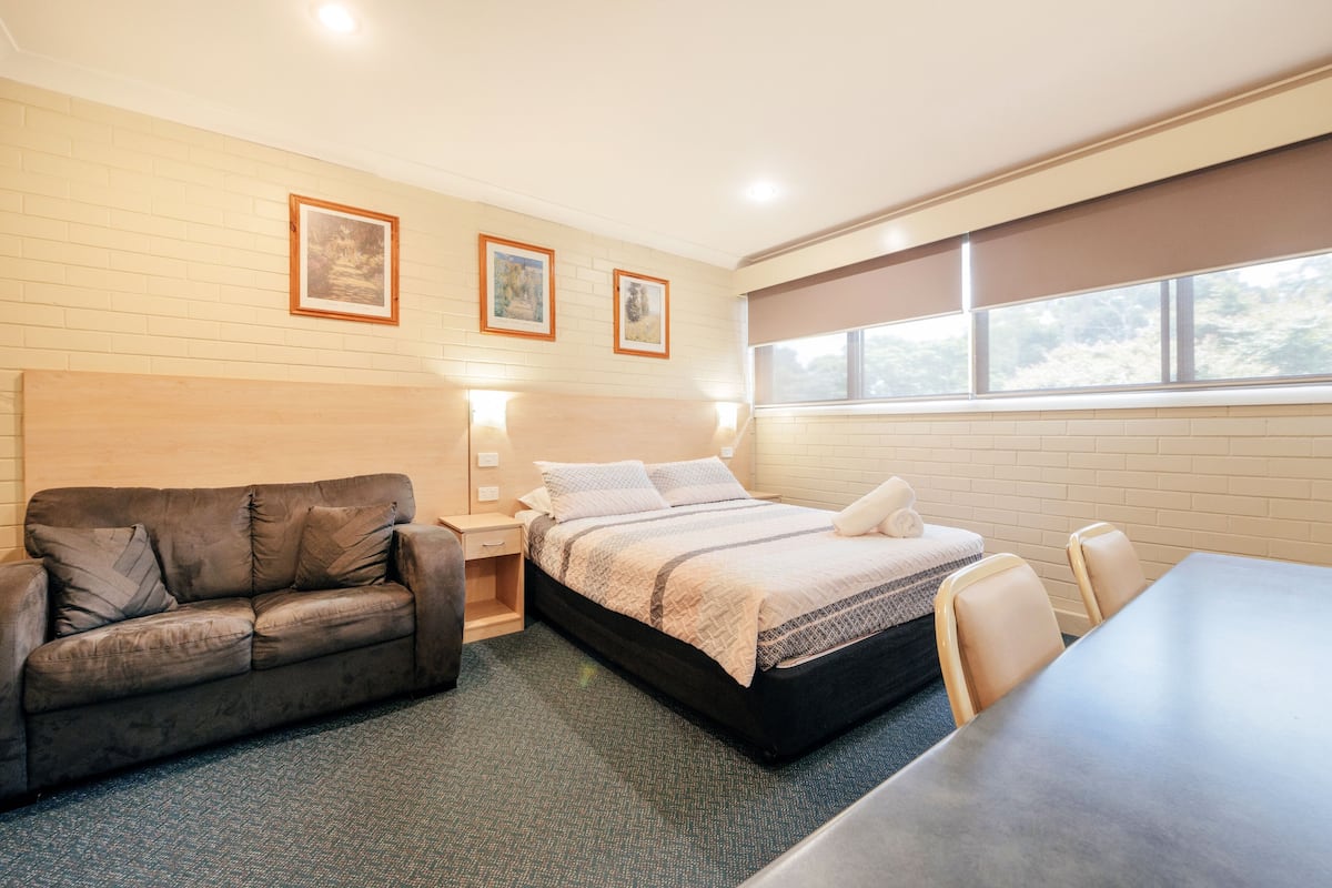 A hotel room with a bed, a sofa, a table, and a window with a view.