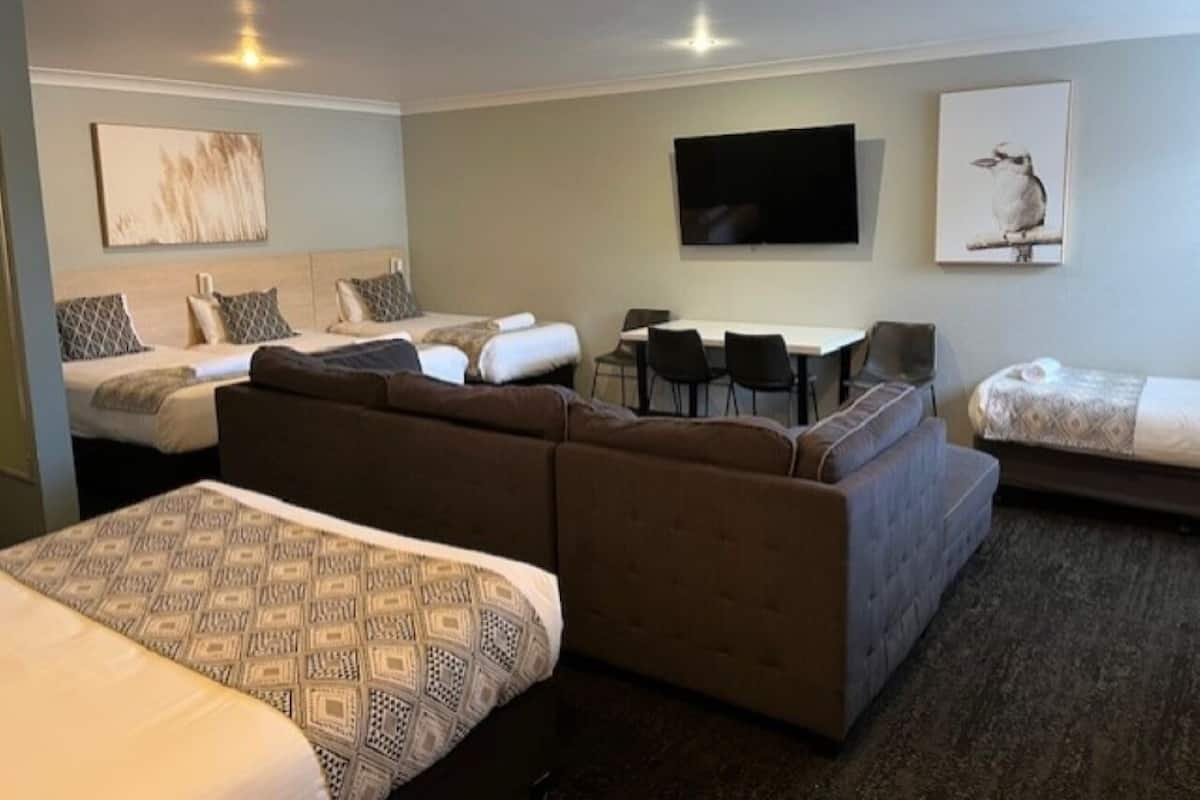 A hotel room with a large bed, a sofa, a small table, and a TV mounted on the wall.