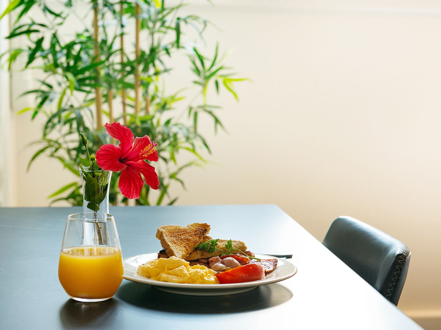 A breakfast table with toast, scrambled eggs, tomatoes, and a glass of orange juice.