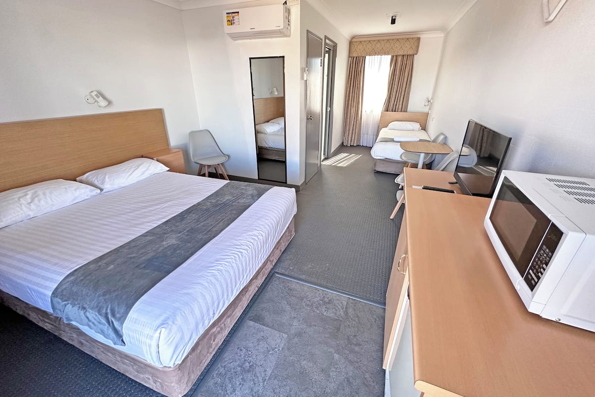 A hotel room with a large bed, a desk with a microwave, a chair, and a TV.