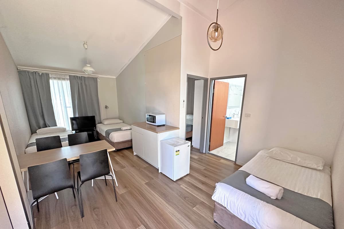 A compact hotel room with a bed, a desk with chairs, a microwave, and a small refrigerator.