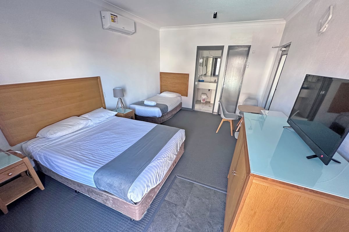 A hotel room with a large bed, a desk with a flat-screen TV, a chair, and a small table.