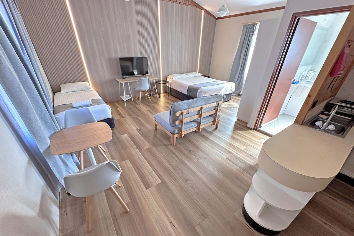 A modern hotel room with a bed, seating area, TV, and a small table.